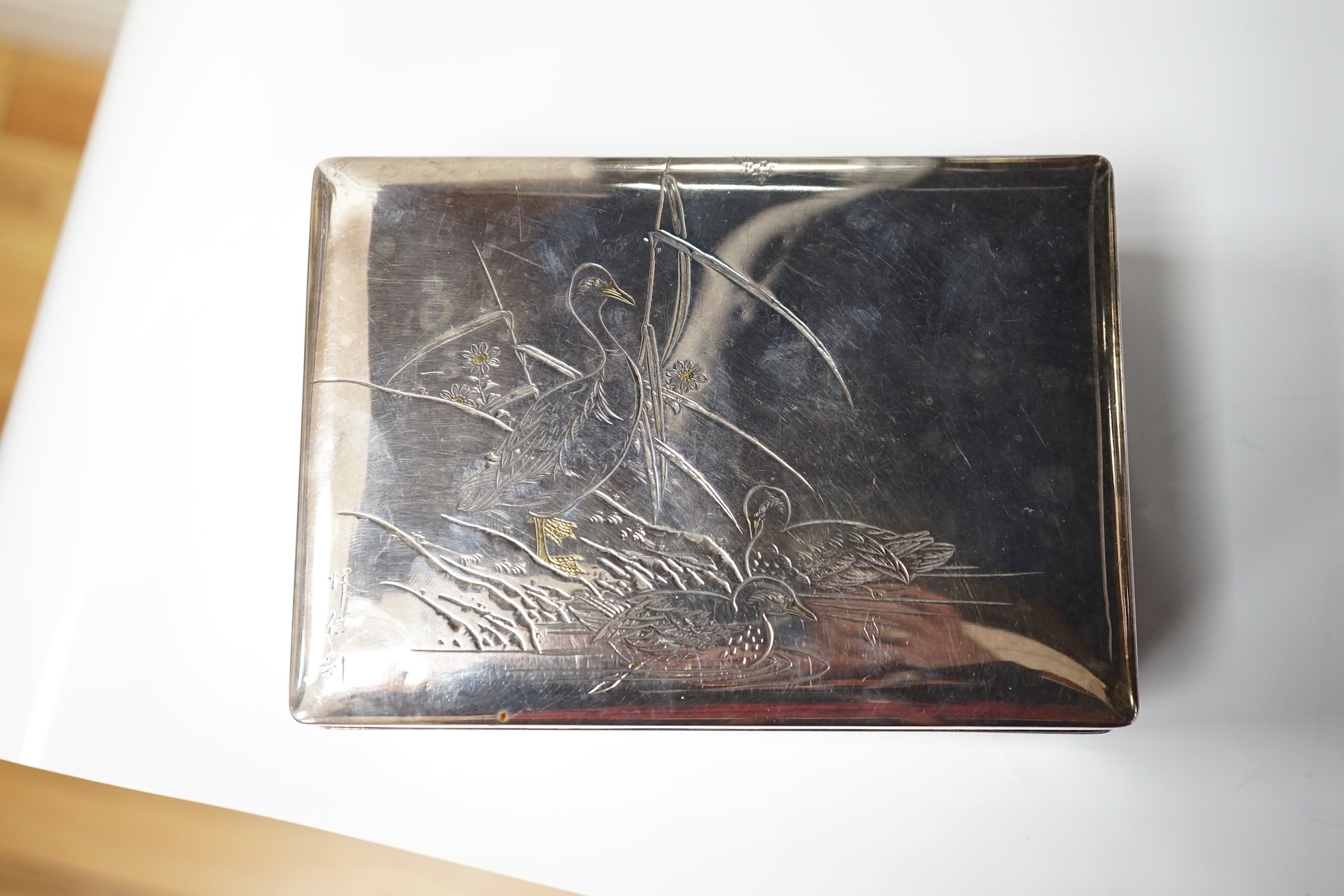 A Japanese white and yellow metal mounted rectangular cigarette box, engraved with birds and reeds, signed to the base, 14.2cm. Condition - fair